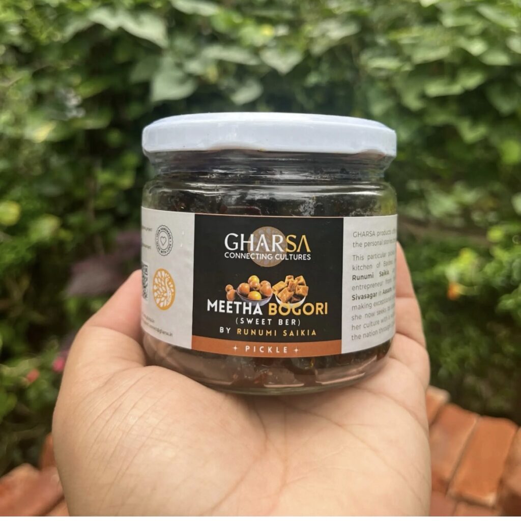 A jar of GHARSA Meetha Bogori pickle held in hand in a garden in Assam
